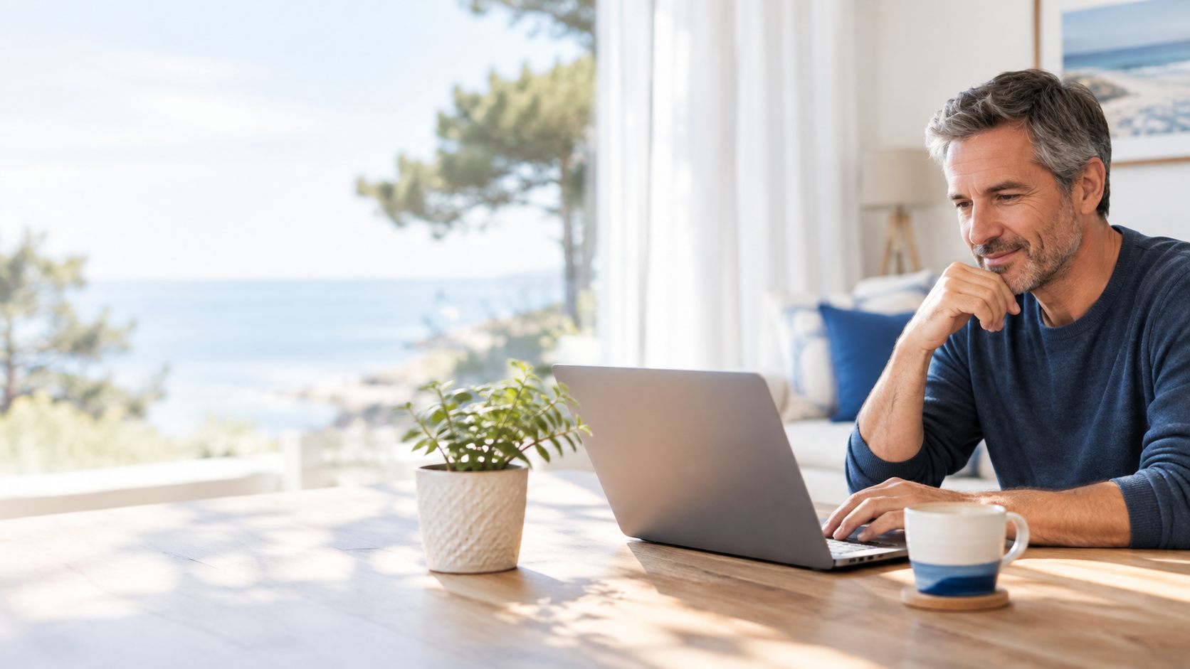Un particulier devant son ordinateur portable, dans un salon lumineux face à la mer